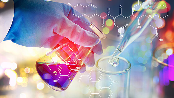 A gloved hand holds a flask while a pipette drops liquid into another container.