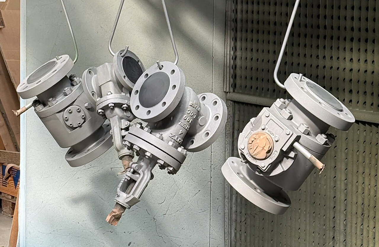 Three gray industrial valves hanging from hooks against a textured background.