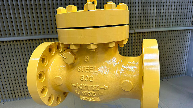 Steel valve with flanged connections, painted bright yellow, suspended for display.