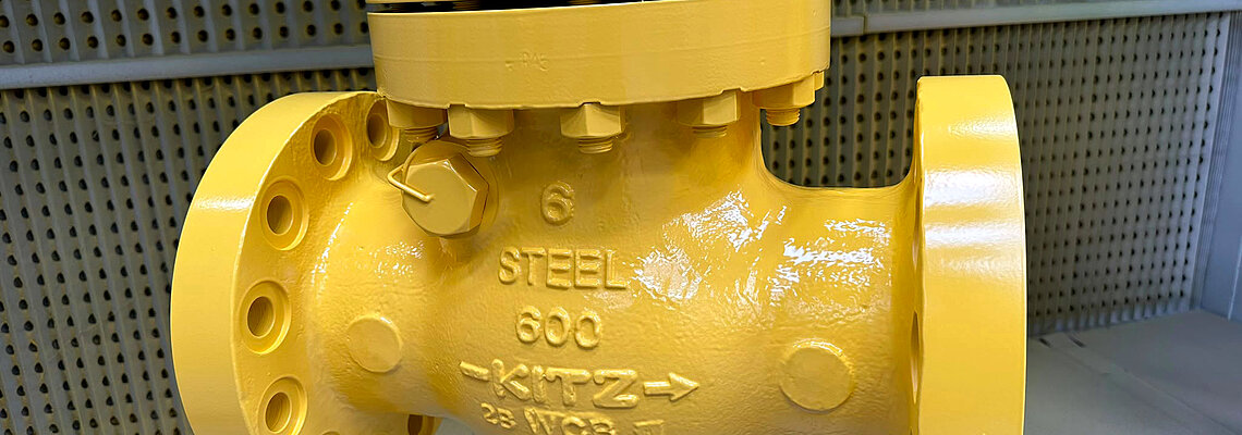 Steel valve with flanged connections, painted bright yellow, suspended for display.