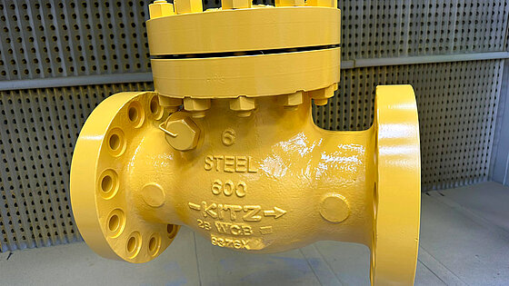 Steel valve with flanged connections, painted bright yellow, suspended for display.
