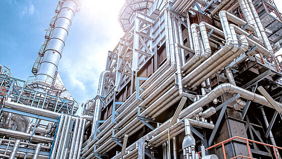 Industrial complex with large metal pipes and structures under bright sunlight.