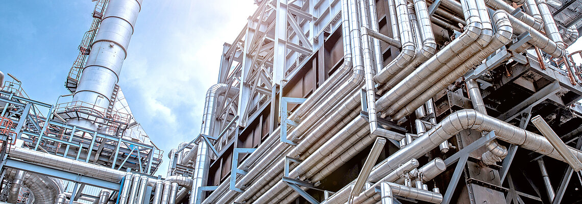 Industrial complex with large metal pipes and structures under bright sunlight.