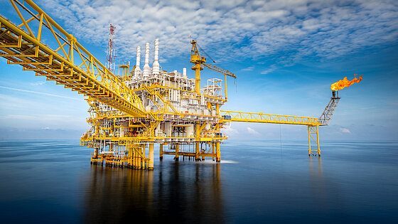 Offshore oil platform with pipelines and a flare stack over water.