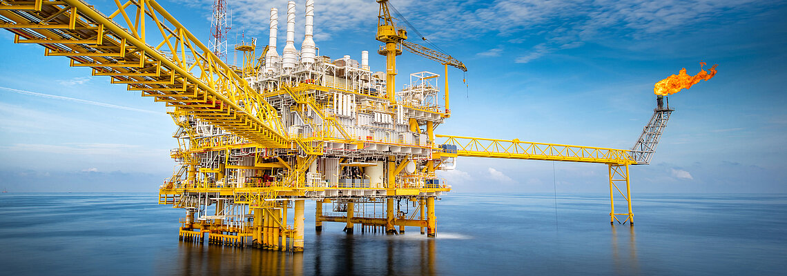 Offshore oil platform with pipelines and a flare stack over water.